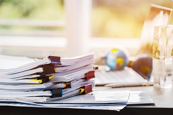 Stack of documents with binder clips on a desk near a laptop and small globe.