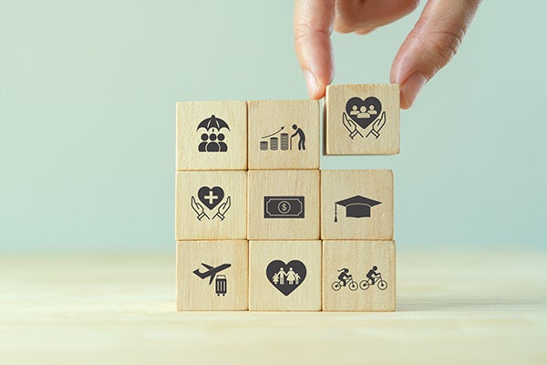 Hand stacking wooden blocks with icons representing health, finance, education, family, and lifestyle.