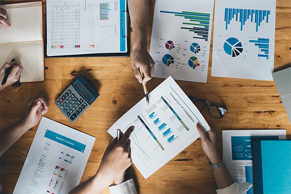 People reviewing financial charts and graphs at a table with documents, calculator, and notebooks.