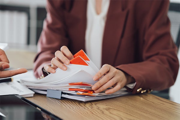 Person in a maroon blazer organizing a stack of documents with red and orange folders.
