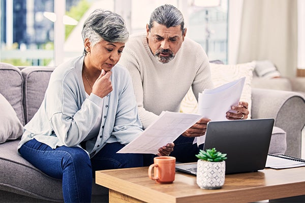 Concerned couple reviewing papers together at home with a laptop and coffee mug on the table.