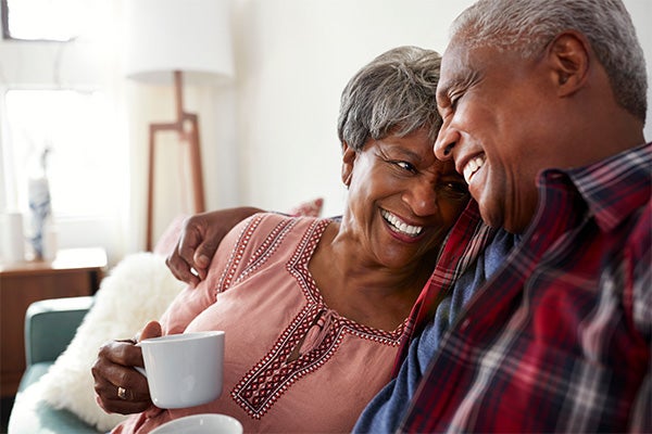 Smiling senior couple sitting close together on a couch, enjoying coffee and each other's company.