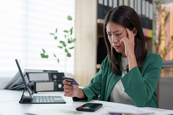 Asian businesswoman frowns at her credit card in her office