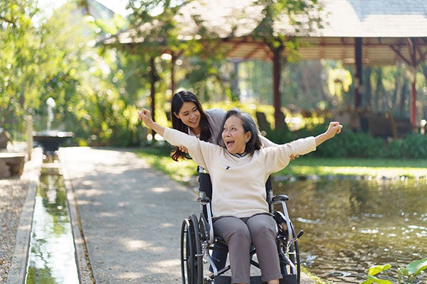 asian daughter pushes her happy mom in a wheelchair in an garden