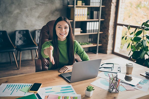 cheerful female boss reaches her hand out to shake your hand over office desk