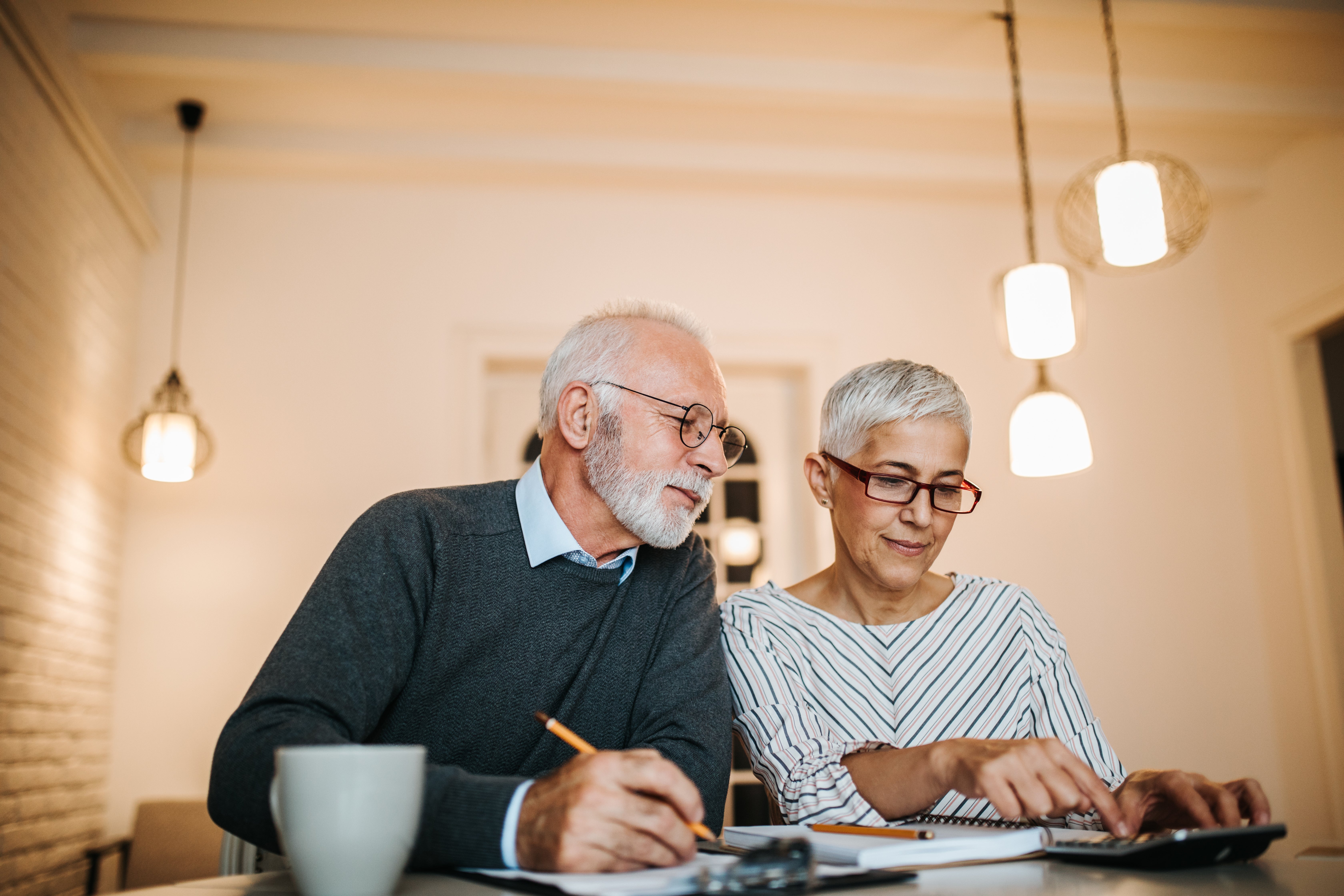 An older couple sitting at a table, reviewing documents together with a calculator, appearing focused and engaged in financial planning.
