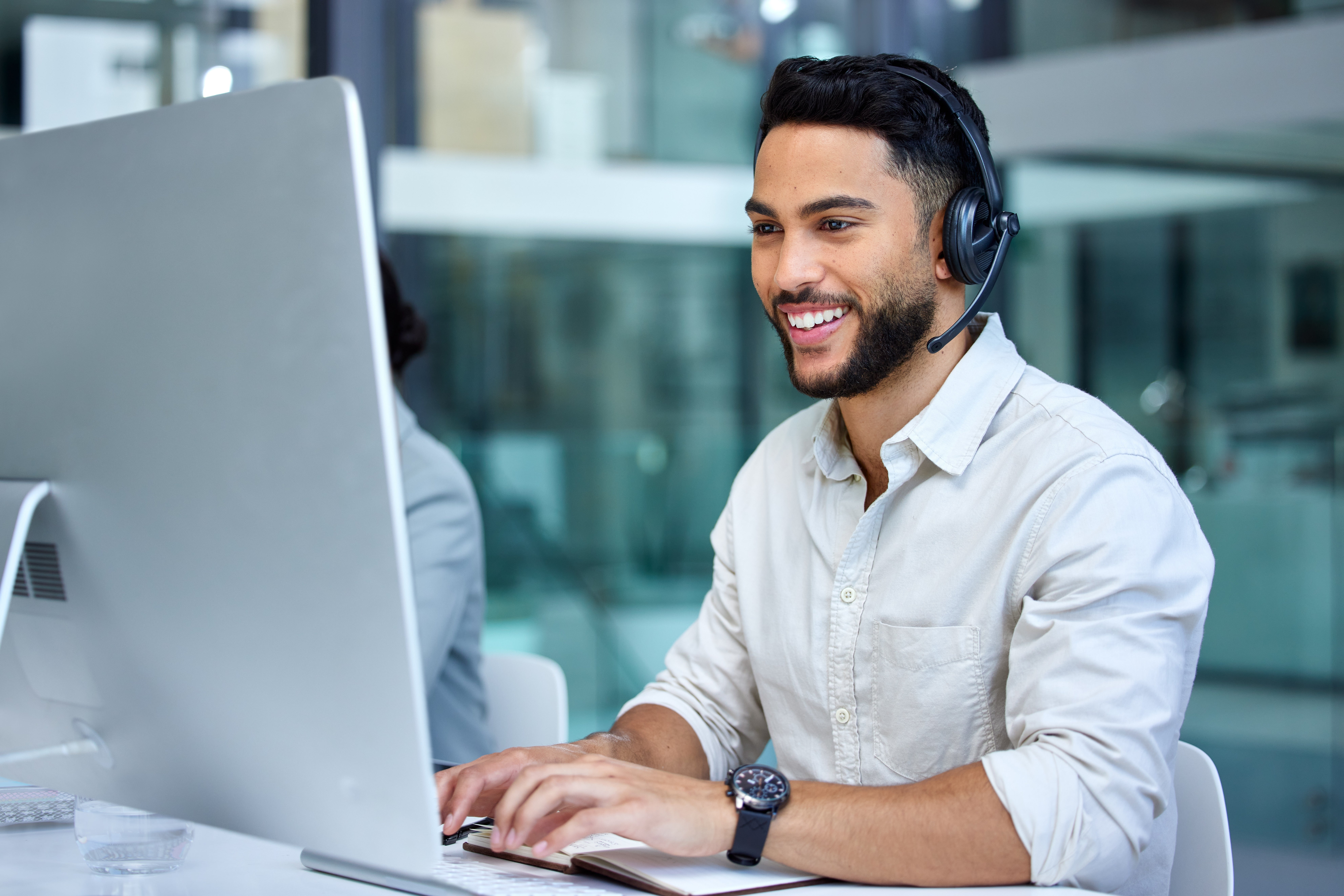 Call center employee with phone headset on looking at computer screen with hands on keyboard