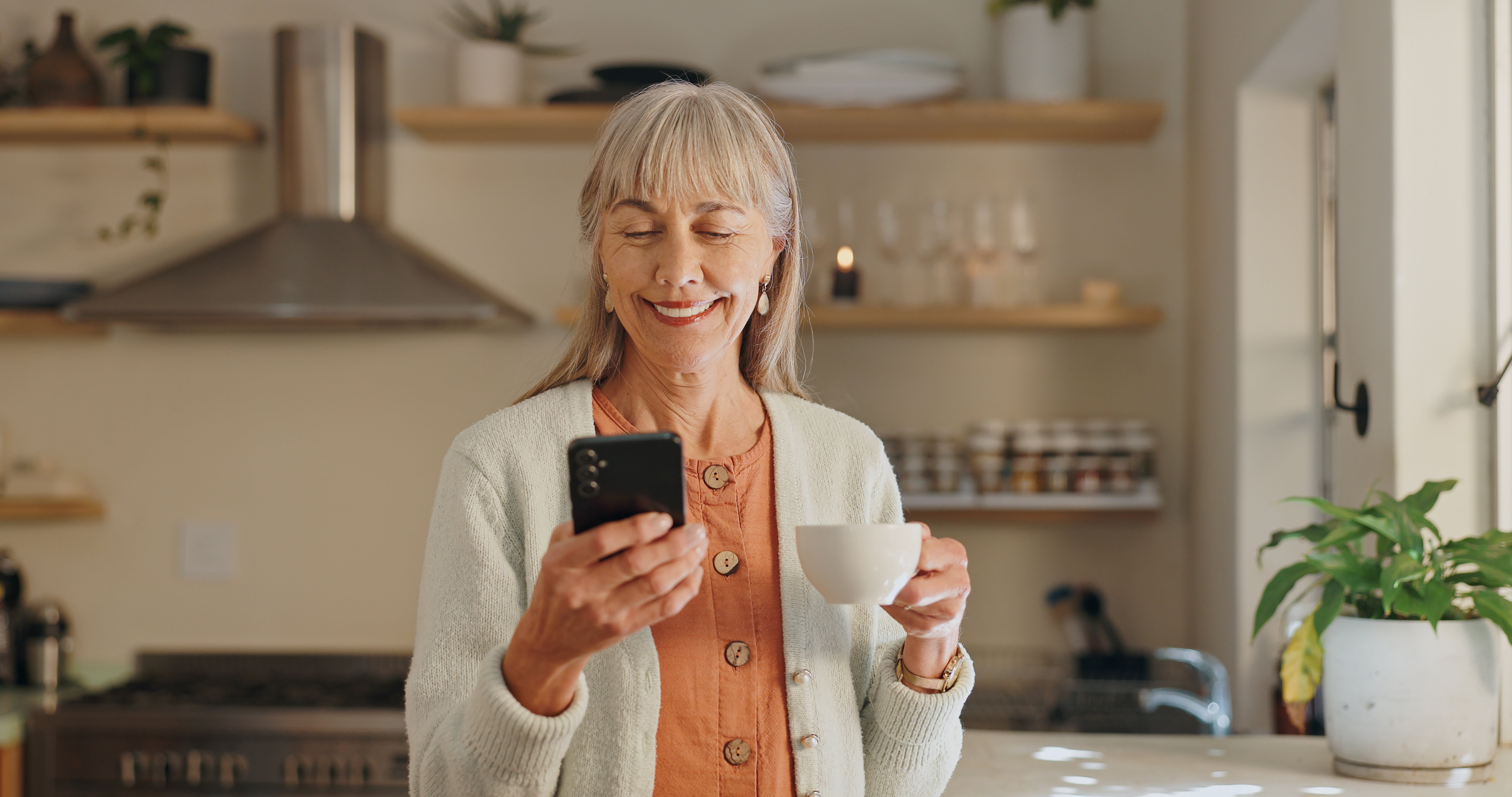 Person looking at phone in kitchen holding cup.